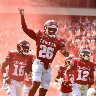 Temple football players in red jerseys celebrating on field during game